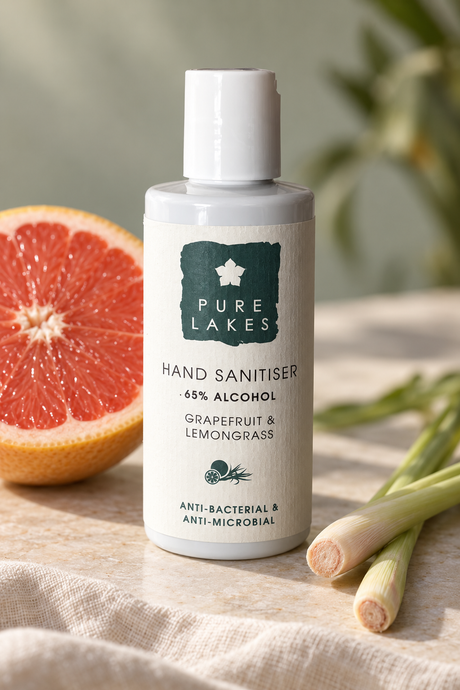 A bottle of Pure Lakes Hand Sanitiser with grapefruit and lemongrass scent, styled on a linen surface with a grapefruit slice and lemongrass stalks in the background.