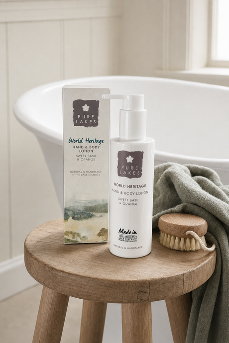 Pure Lakes World Heritage Hand & Body Lotion bottle and box displayed on a wooden stool next to a green towel in a bright bathroom setting.