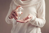 Person applying a white spray bottle to their hand against a neutral background