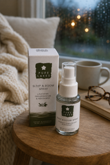Pure Lakes Sleep & Room Spray bottle and its box displayed on a wooden table next to a mug, with a cozy blanket and a blurred window in the background.