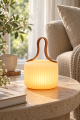 Mochi Pure lamp with a brown carry strap on a pale stone side table beside a linen armchair.