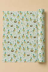 A roll of wrapping paper unrolled to show a repeating pattern of small penguin characters in green and orange on a Duck Egg Blue background, set against a solid beige backdrop.