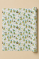 A roll of wrapping paper with a dense pattern of illustrated birds in green, yellow, and brown on an off-white background, shown against a solid beige backdrop.
