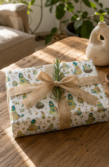 A wrapped gift box on a rustic wooden table, covered in cream wrapping paper with a whimsical green and blue Duck character print, tied with a natural burlap ribbon and a small green sprig.