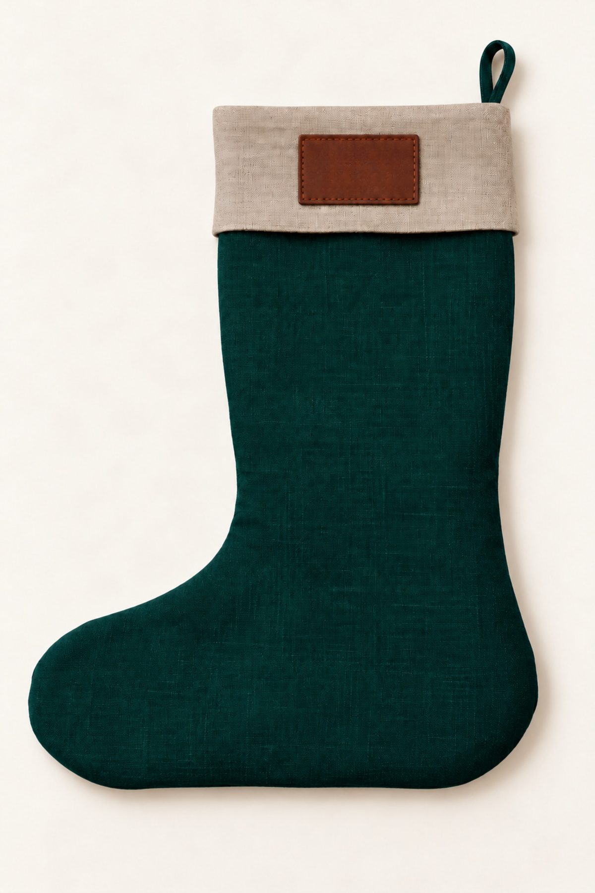 A dark green linen Christmas stocking with a light beige fabric cuff and a brown rectangular patch on the front, shown against a plain off-white background.