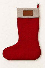 A festive linen Christmas stocking with a vibrant red body and a natural linen fabric cuff featuring a brown leather patch, shown against a plain off-white background.