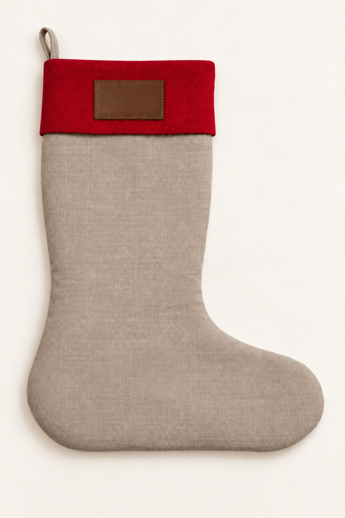 A linen Christmas stocking with a natural linen body, a vibrant red linen cuff, and a brown leather patch on the cuff, shown against a plain off-white background.