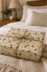 Christmas wrapping paper featuring red-breasted birds perched among holly leaves, red berries, rosehips, leafy sprigs, bare winter twigs and small golden stars. The illustrated repeat uses deep green, berry red, warm brown and soft grey on a warm cream background.