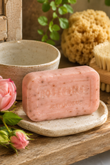 Rose bar of soap on a stone plate with a wooden background, featuring a plant and sponge.