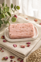 Pink rose soap bar on a white plate with dried flowers and green leaves in the background