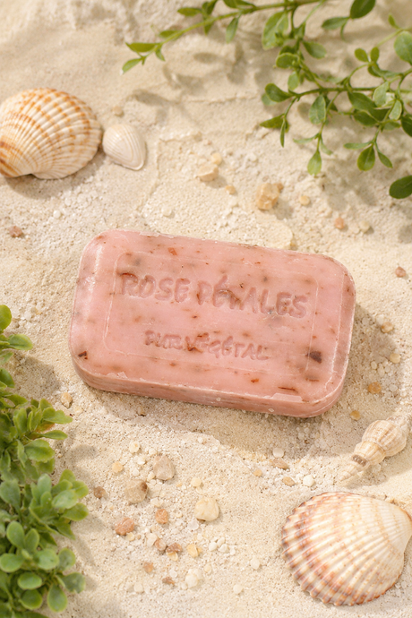 Bar of soap with 'Rose Perles' branding on a sandy background with shells and plants.