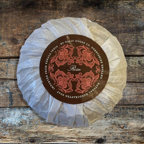 Round of soap rose scented with a decorative brown label on a wooden surface