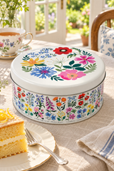 A round floral tin cake box with a powdered sponge cake and jam filling, shown on a  table in a bright kitchen 