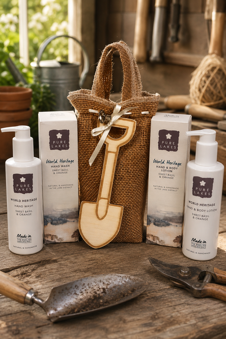 A gift set from Pure Lakes featuring hand wash and body lotion bottles, two product boxes, a burlap tote bag, and a wooden shovel-shaped keychain, arranged on a rustic wooden table with gardening tools.