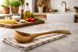 Wooden ladle on a kitchen counter with a view of a kitchen in the background.