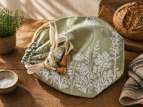 Sage Green Linen Bread bag with white floral patterns on a wooden table with bread and a plant.