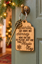 A wooden Christmas door key tag hanging from a brass doorknob on a green door, with a decorative antique-style brass key attached. The tag is engraved with the phrase 'Santa, WE HAVE NO CHIMNEY HERE YOU SEE SO PLEASE JUST USE THIS Magic Key' and a snowflake design.