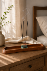 Incense sticks on a wooden tray with a plant and curtain in the background