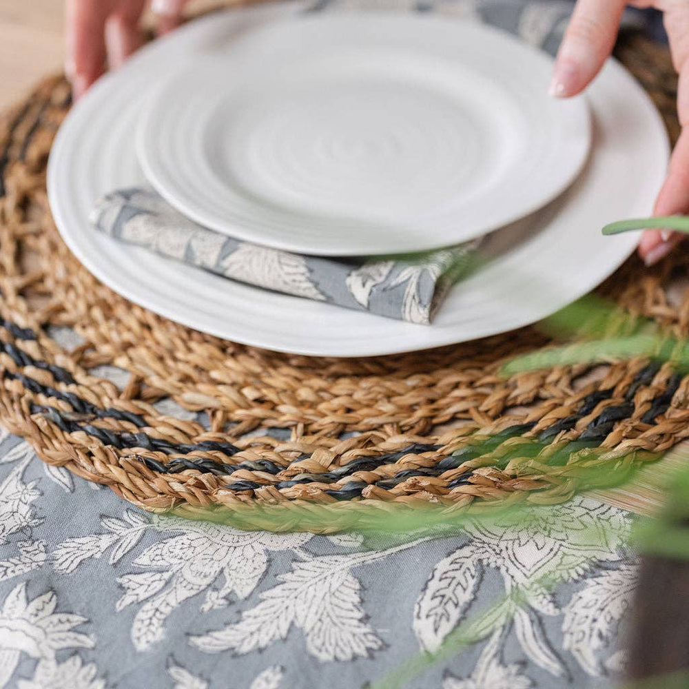White plates stacked on a woven placemat with a floral tablecloth underneath
