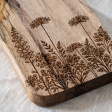Wooden cutting board with floral engraved designs on a table setting.
