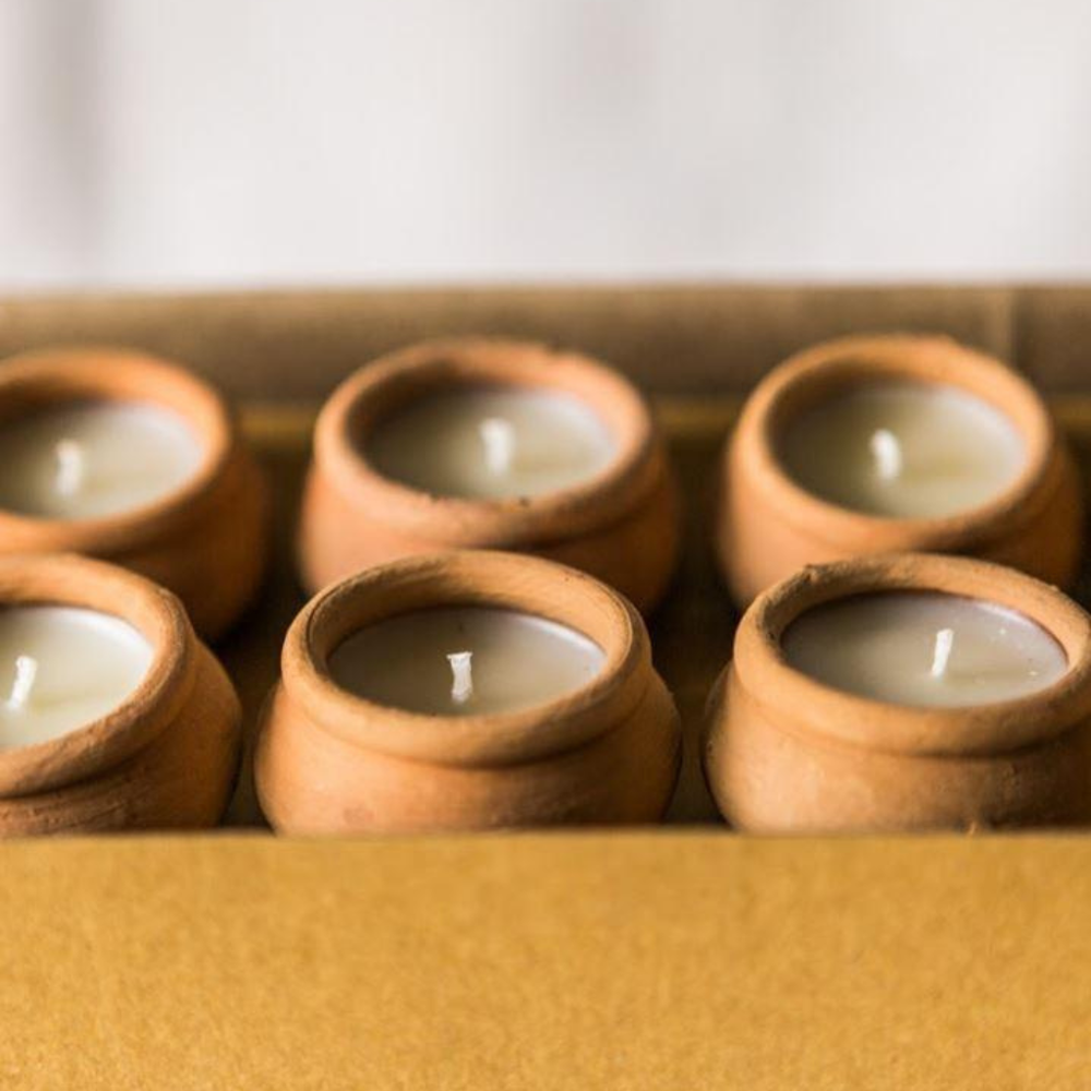 Set of 10 small candles in terracotta holders on a wooden surface.