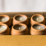 Set of 10 small candles in terracotta holders on a wooden surface.