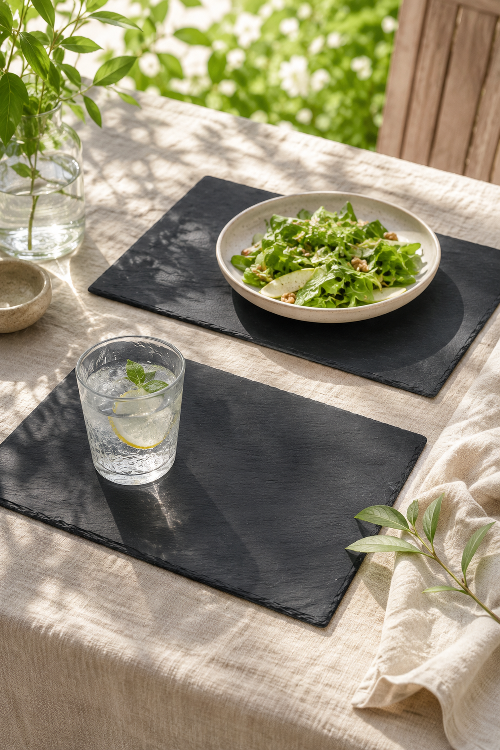 Table setting with a bowl of salad and a glass of water on Set of 2 rectangular slate placemats and serving platters made from natural slate with rustic edges.