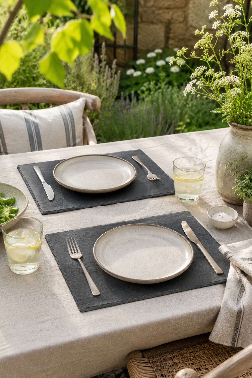Set of 2 rectangular slate placemats and serving platters made from natural slate with rustic edges. Outdoor dining setup with plates, glasses, and cutlery on a table with a garden view.