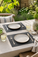 Set of 2 rectangular slate placemats and serving platters made from natural slate with rustic edges. Outdoor dining setup with plates, glasses, and cutlery on a table with a garden view.
