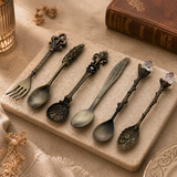 Set of decorative spoons on a stone surface with a book and candle in the background
