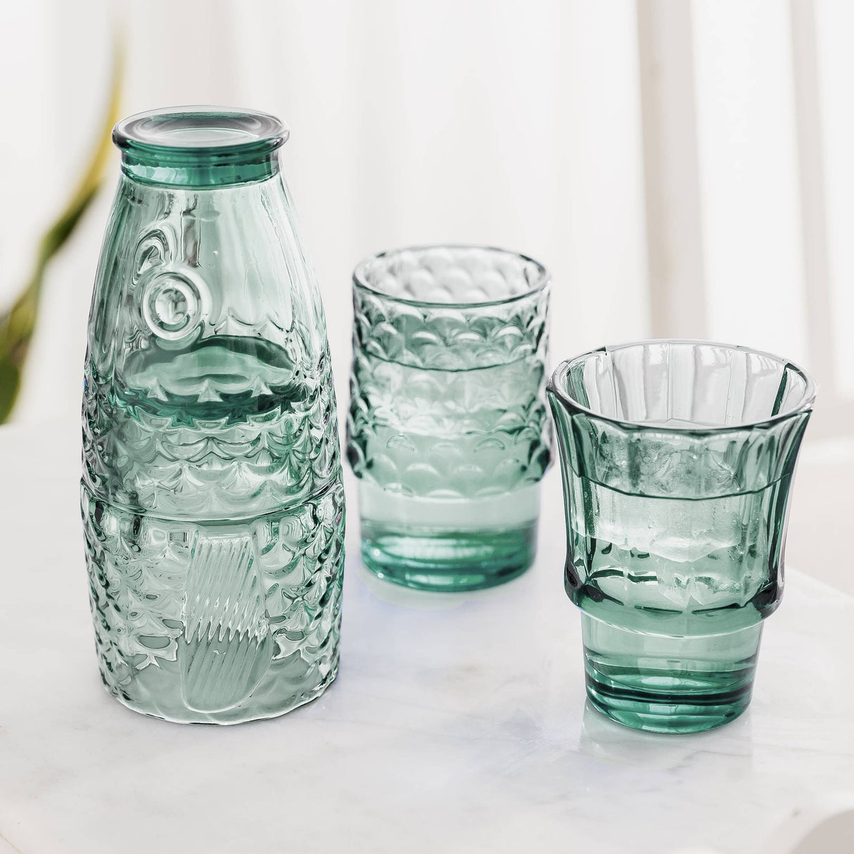 Set of green glass tumblers on a light background that make a fish when stacked together