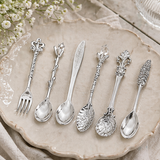 Set of decorative silver spoons and forks on a table with a bowl of cereal and a cup of tea.