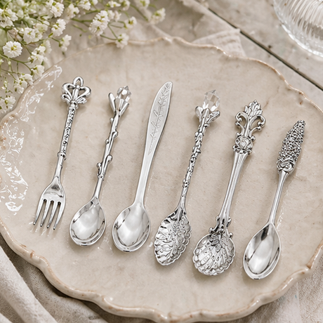 Set of decorative silver spoons and forks on a table with a bowl of cereal and a cup of tea.
