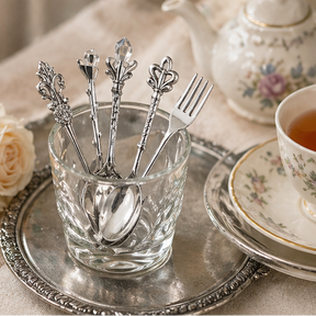 Set of decorative silver spoons and forks on a table with a bowl of cereal and a cup of tea.