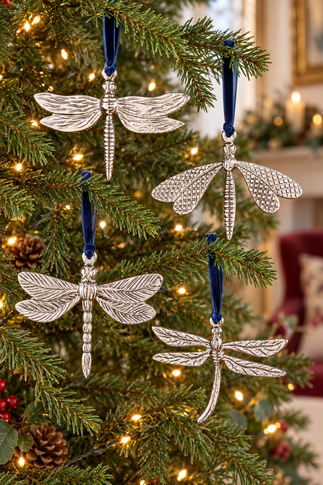 Four silver dragonfly ornaments with textured wings and blue ribbons hang on a decorated Christmas tree with warm lights.