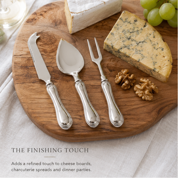 Silver cheese knife, server, and fork set on a wooden board with cheese and grapes.