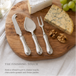 Silver cheese knife, server, and fork set on a wooden board with cheese and grapes.