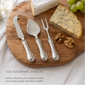Silver cheese knife, server, and fork set on a wooden board with cheese and grapes.