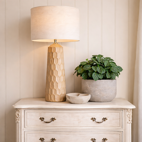 Decorative lamp, plant, and bowls on a white dresser against a beige wall.
