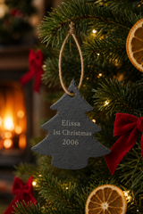 A dark gray slate Christmas tree ornament engraved with 'Elissa 1st Christmas 2006' hanging on a decorated Christmas tree with red bows, dried orange slices, and warm lights.