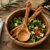 Wooden salad bowl with a salad and two wooden spoons on a wooden surface.