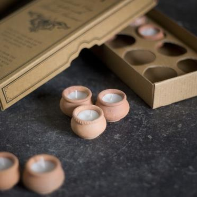 Small terracotta pots with candles inside on a dark surface with an open cardboard box.