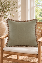 Square sage linen cushion with gathered natural edging resting on a wooden cane armchair.