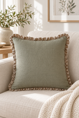 Square sage linen cushion with a natural ruffle on an oatmeal sofa beside a knitted cream throw.