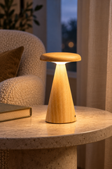 A small mushroom-shaped table lamp made of natural wood, glowing with warm light on a stone side table in a cozy living room setting.