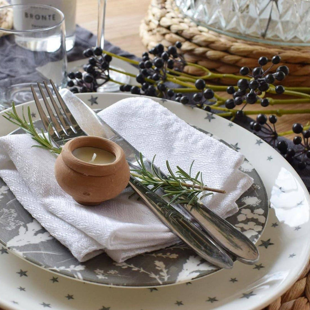 Table setting with a plate, fork, knife, candle, and rosemary sprig on a woven placemat.