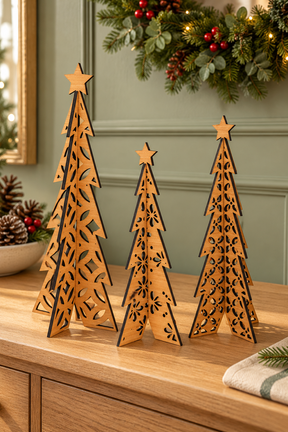 Three laser-cut wooden Christmas tree ornaments with star toppers, displayed on a wooden cabinet in a decorated holiday setting.