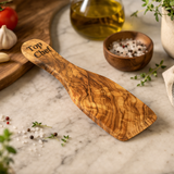 Wooden spatula with 'Top Chef' text on a marble surface with kitchen items.