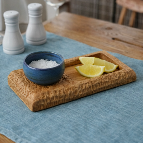 wooden tray with a blue bowl containing lemon slices and spices on a table.