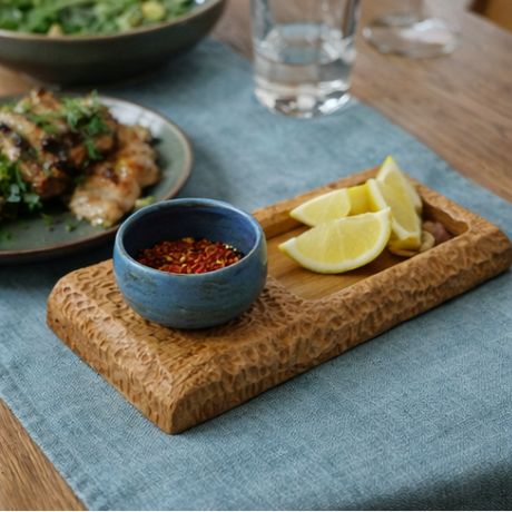 wooden tray with a blue bowl containing lemon slices and spices on a table.